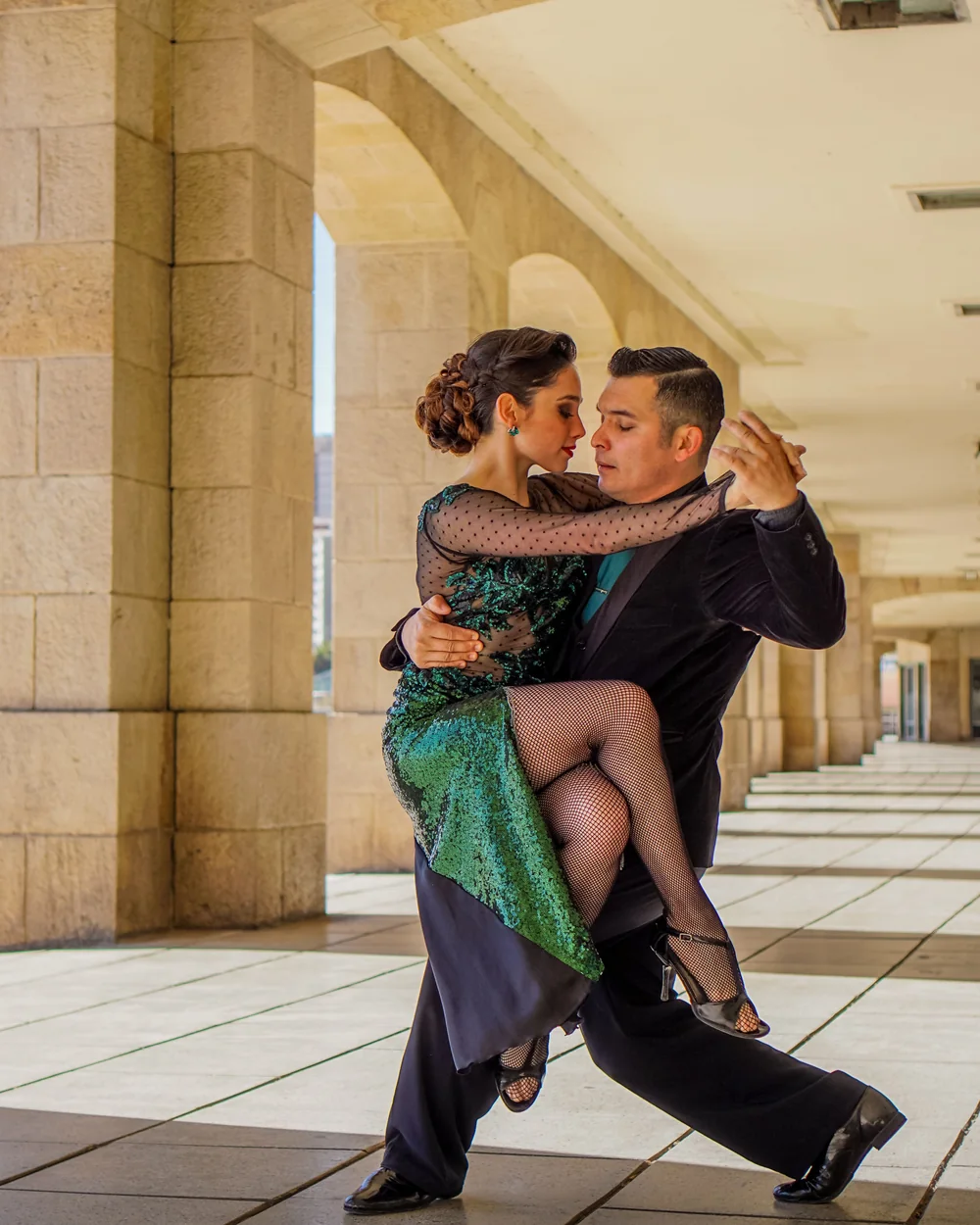 A tango couple mid-turn, the woman in a sequinned green dress (representative photograph of Argentine/Uruguayan tango, not Primuseum itself)